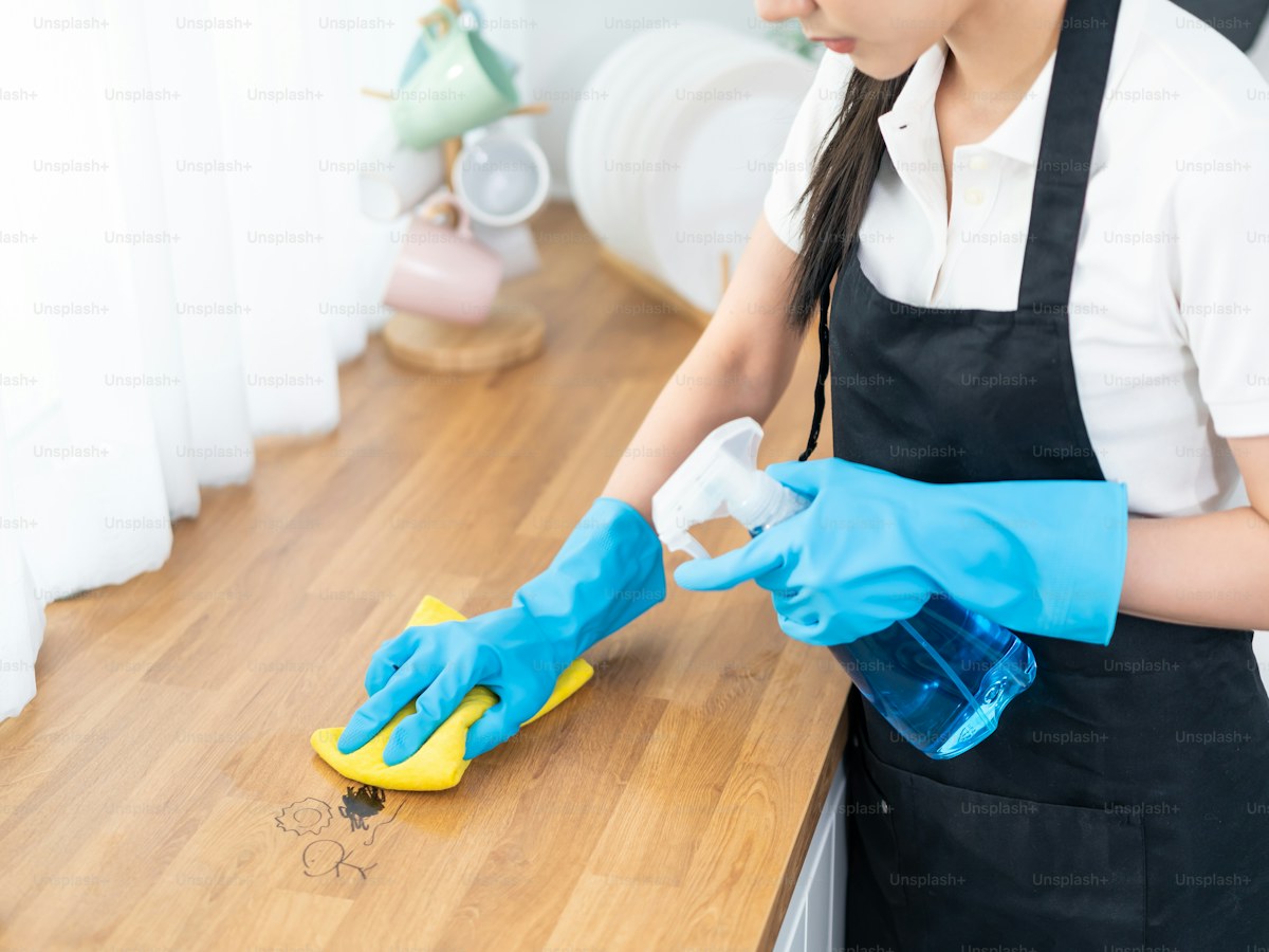A person in a black apron and blue gloves cleaning a wooden countertop