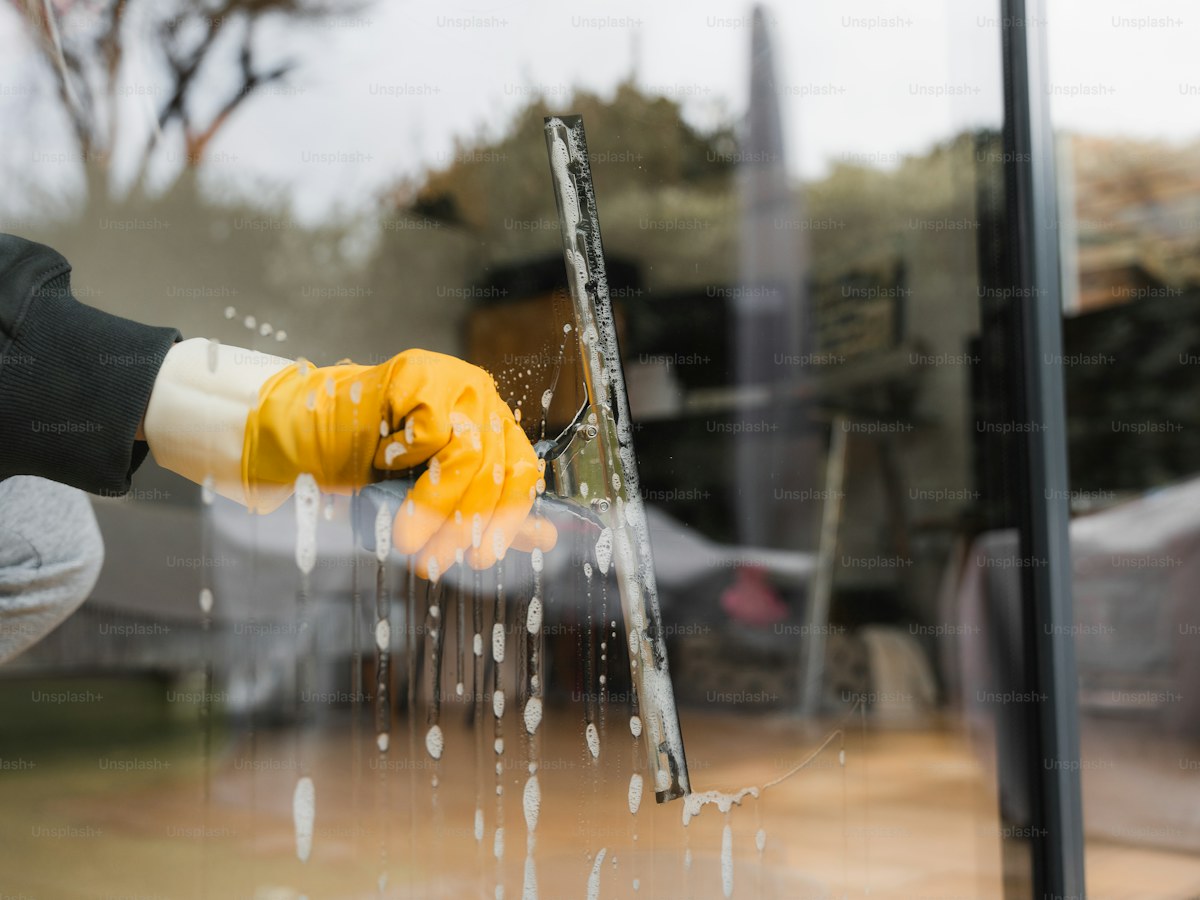 a person wearing yellow gloves is washing a window